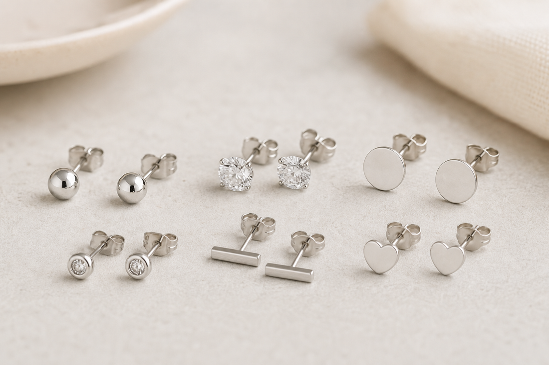 Several simple stud earrings in silver and gold tones arranged on a neutral surface