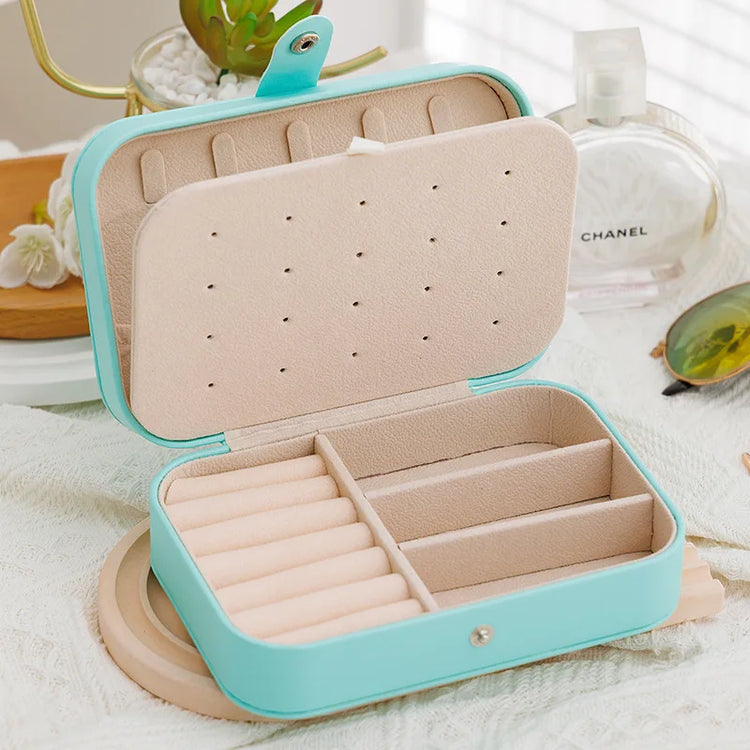 Leather travel jewelry box with button closure and compartments for rings, earrings, and bracelets